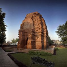 a bench sitting in the middle of a park next to a tall brick structure with carvings on it