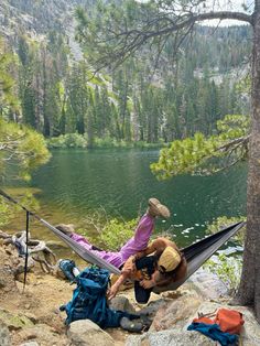 a man sitting in a hammock on top of a rock next to a lake