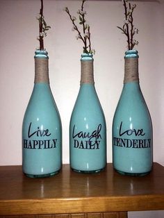 three blue bottles with flowers in them sitting on a wooden table next to a white wall