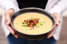 a person holding a bowl of soup with bacon and green onions on top in their hands