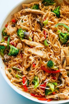 a bowl filled with noodles, broccoli and other veggies on a white surface