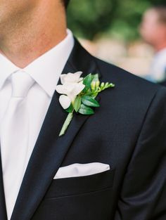 a man wearing a black suit and white flower boutonniere on his lapel