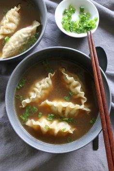 two bowls filled with dumplings next to chopsticks on a gray table cloth