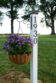 a planter hanging from the side of a white pole with purple flowers in it