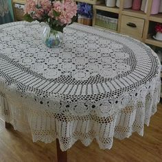 a white doily tablecloth with pink flowers in a vase on top of it