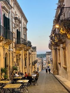 people are sitting at tables on the side walk in an old european city with stone buildings and balconies