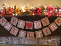 a banner that says be my valentine hanging from a fireplace mantel with flowers on it