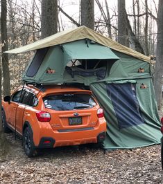 an orange subarunt parked in the woods with its roof tent up on it