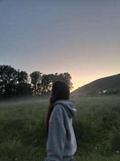 a person standing in a field with trees and fog on the ground at sunset or dawn