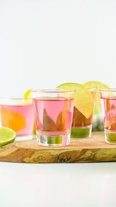 three shot glasses filled with pink, green and yellow drinks on top of a wooden cutting board