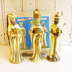 three golden figurines sitting next to each other on top of a white table