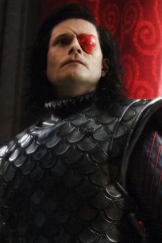 a man in black leather armor with red eye patches on his face and chest, looking to the side