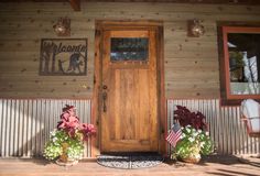 two potted plants are sitting in front of a wooden door with welcome sign on it