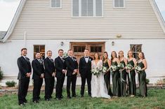 a group of people standing in front of a white building with green and black dresses