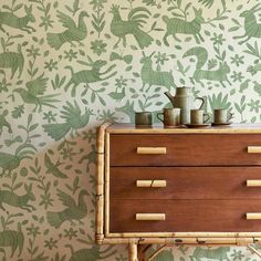 a wooden dresser with two vases on top of it next to a wallpaper