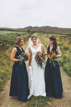 three bridesmaids walking down a dirt path in their wedding gowns and bouquets