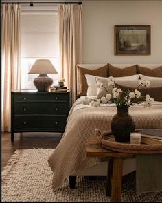 a bedroom with a bed, nightstands and flowers in a vase on the end table