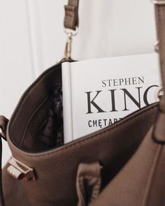 a book is sitting in the pocket of a brown handbag on a white wall