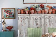 an old cabinet is covered with potted flowers and other decorative items in front of a painting on the wall