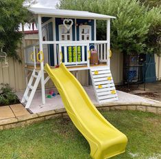 a yellow slide in front of a blue and white house with a play structure behind it