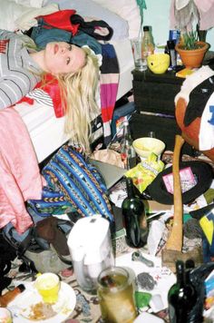 a woman laying on top of a bed surrounded by clutter and bottles in a room