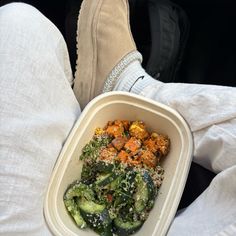 a person holding a container with food in it on their lap and wearing white pants