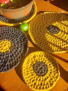 three crocheted coasters sitting on top of a wooden table next to an apple