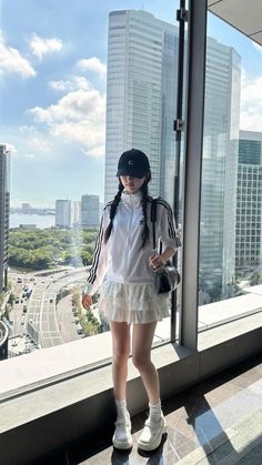 a woman standing in front of a window next to a tall building with lots of windows