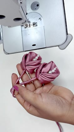 someone is holding two small pink bows in their hand while sewing on the sewing machine