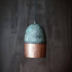 a green and copper pendant light hanging from a metal rod on a gray wall background