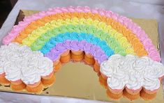 there is a rainbow cake with white frosting on the top and pink, yellow, green, blue, orange, and purple cupcakes in the middle