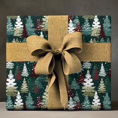 a present wrapped in green and gold paper with a brown bow on the top, surrounded by christmas trees