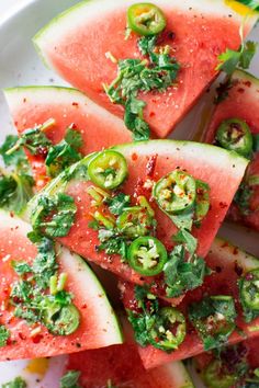 slices of watermelon with herbs and seasoning on top, sitting on a white plate