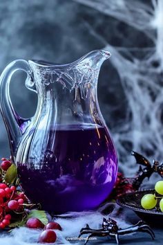 a glass pitcher filled with purple liquid surrounded by berries and spooky spider web