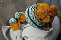 a baby wearing a knitted hat and mittens on top of it's head