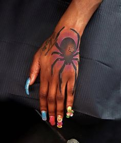 a woman's hand with colorful nail polishes and a spider tattoo on it