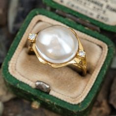 This pretty mabé pearl ring is crafted of 18k yellow ring and features a centered mabé pearl with a diamond accent on each sides. The ring is currently a size 6.25. The pearl is lightly blemished and one of the diamond accents has an unnoticeable chip. Luxury Antique Style Pearl Ring With Cabochon, Luxury Oval Diamond Pearl Ring, Luxury Modern Pearl Engagement Ring, Luxury Classic Pearl Ring With Single Cut Diamonds, Luxury Pearl Ring With Gemstone, Luxury Timeless Pearl Ring, Luxury Oval Heirloom Pearl Ring, Luxury Victorian Oval Pearl Ring, Luxury White Heirloom Pearl Ring