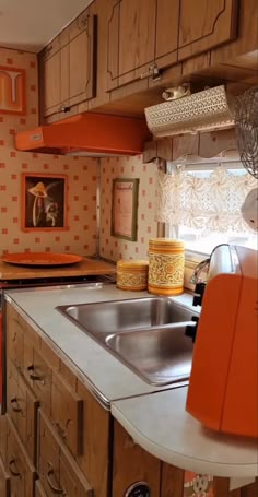 a kitchen with orange and white accessories on the counter top, sink and cabinets in it