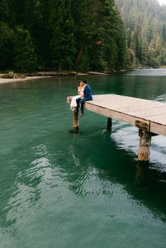 a man and woman sitting on a dock in the middle of a body of water