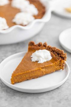 a slice of pumpkin pie on a white plate with whipped cream in the middle and two bowls behind it