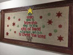 a cross stitch christmas tree is hung on the wall in front of a sign that reads, for unto you is born this day in the city of david and salvation which is christ