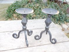 two wrought iron candlesticks sitting on top of a wooden table next to bushes