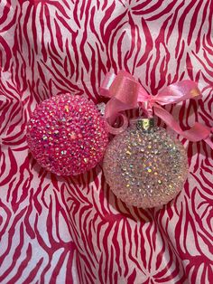 two ornaments are sitting on a pink and white fabric with zebra print pattern behind them