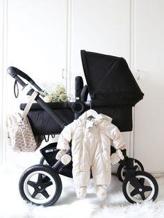 a baby stroller with an infant's winter outfit on it, sitting in front of a white wall