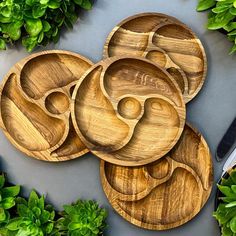 four wooden plates sitting on top of a table next to green plants and a pair of scissors