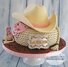 a cowboy hat on top of a cake that is decorated with pink and white ribbon