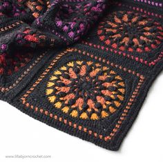 a crocheted blanket is laying on top of a white surface with an orange and purple design