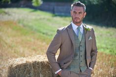 a man in a suit standing next to a bale of hay with his hands on his hips