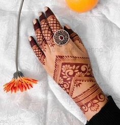 a henna tattoo on someone's hand next to an orange and a flower