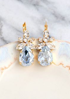 two pairs of gold and crystal earrings on a marble plate with white marble countertop